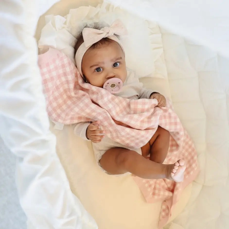 Baby wrapped in a pink checkered plaid blanket with a pacifier, wearing a headband.